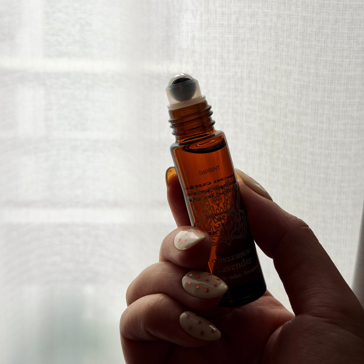 Hand holding a small brown rollerball bottle against a white background