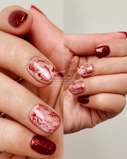 Close-up of hands with red and white marbled nail art on a neutral background