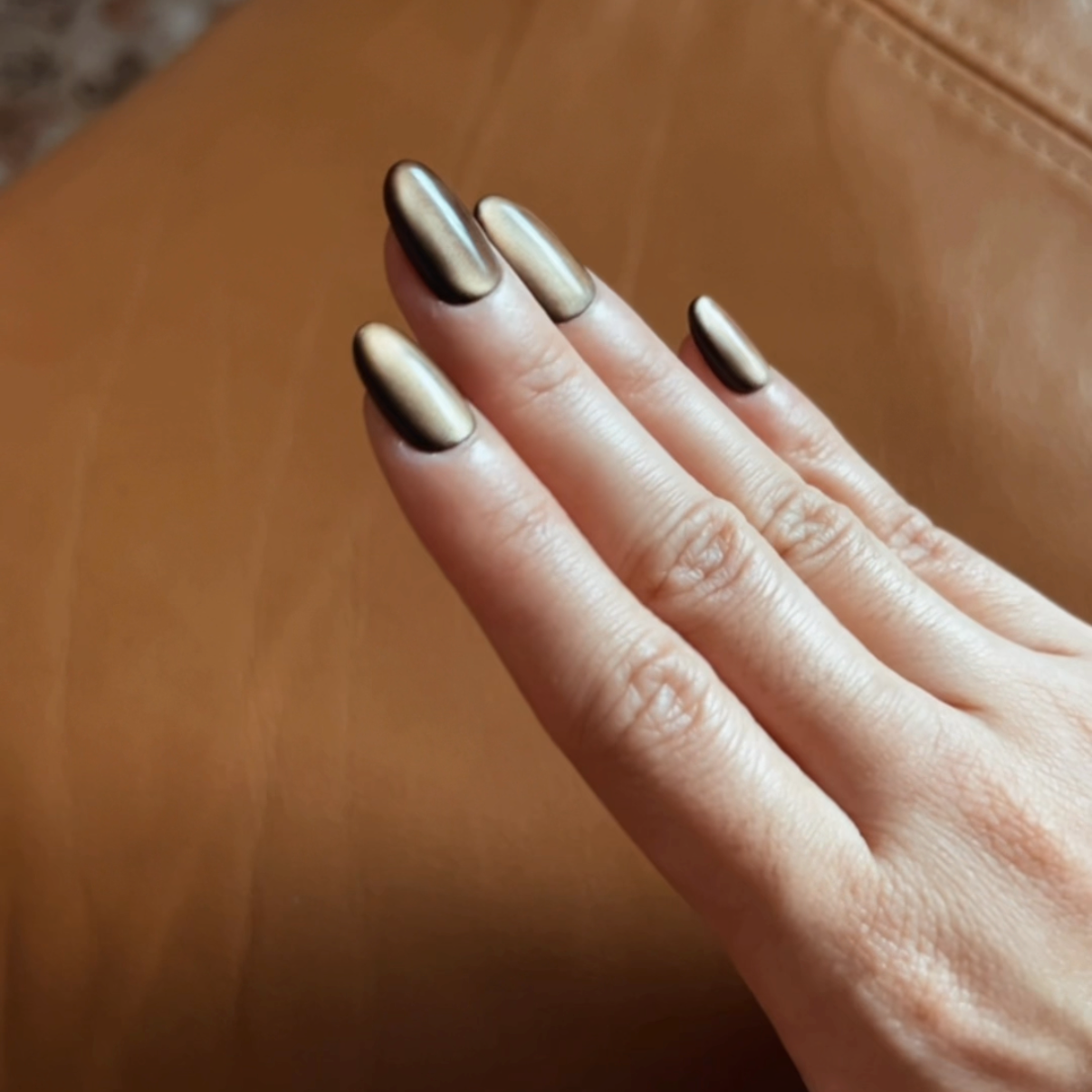 Hand with dark brown cat eye effect nail polish on a brown leather background