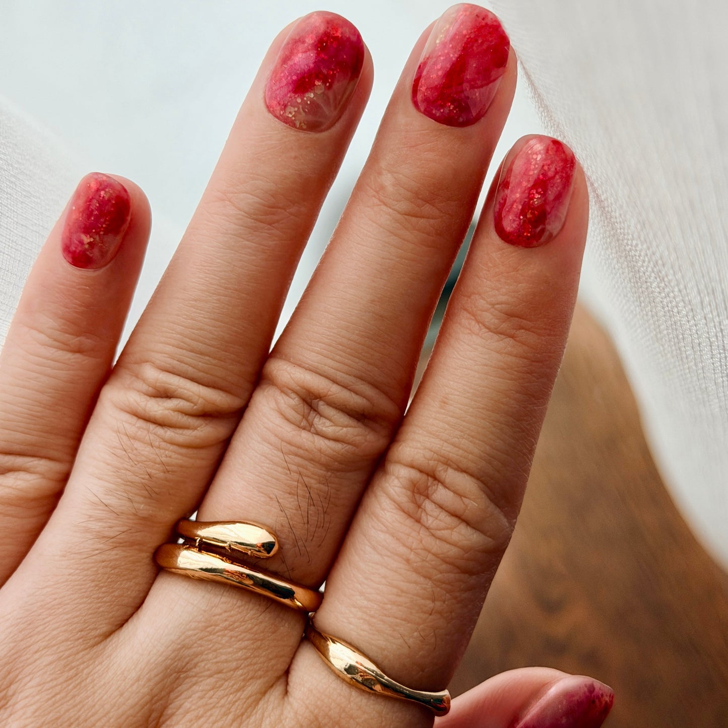 Hand with gold rings and marbled nails on a neutral background