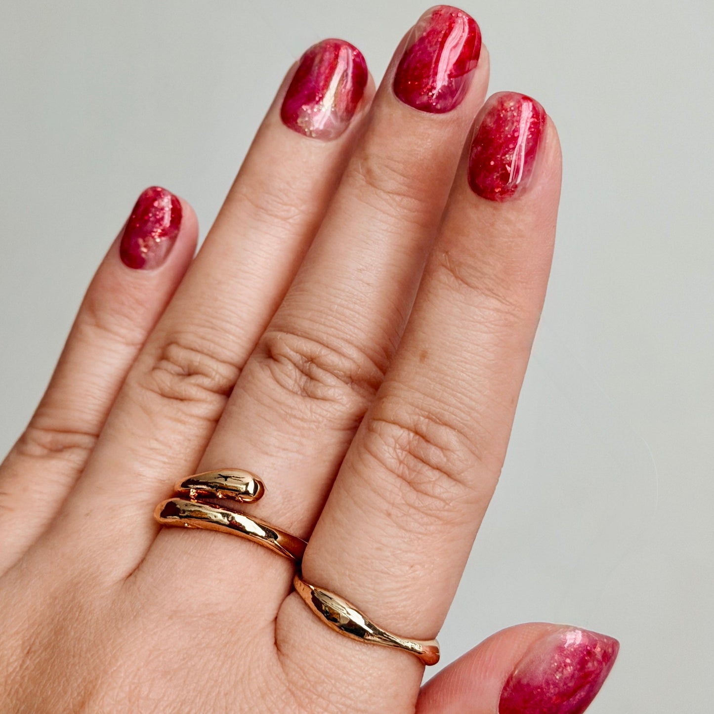 Hand with gold rings and red marbled press-on nails on a neutral background