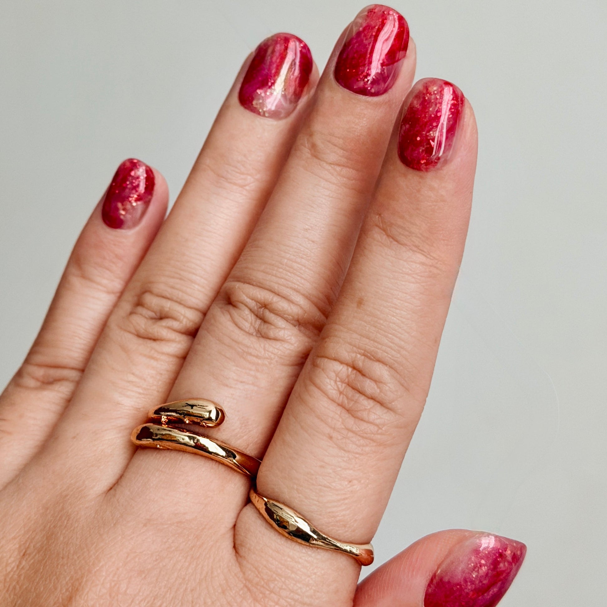 Hand with gold rings and red marbled press-on nails on a neutral background