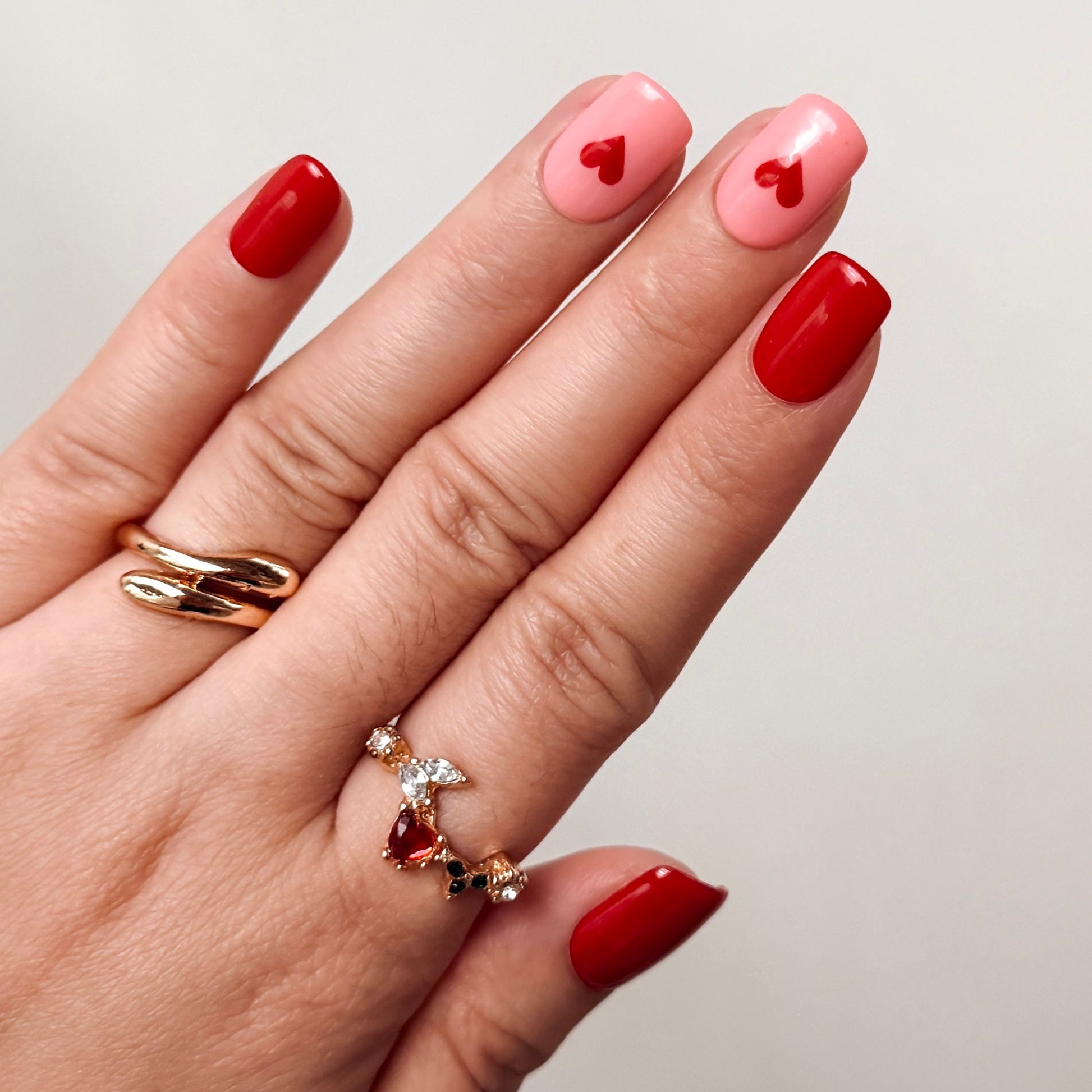 Hand with red and pink nail polish wearing gold rings on a neutral background