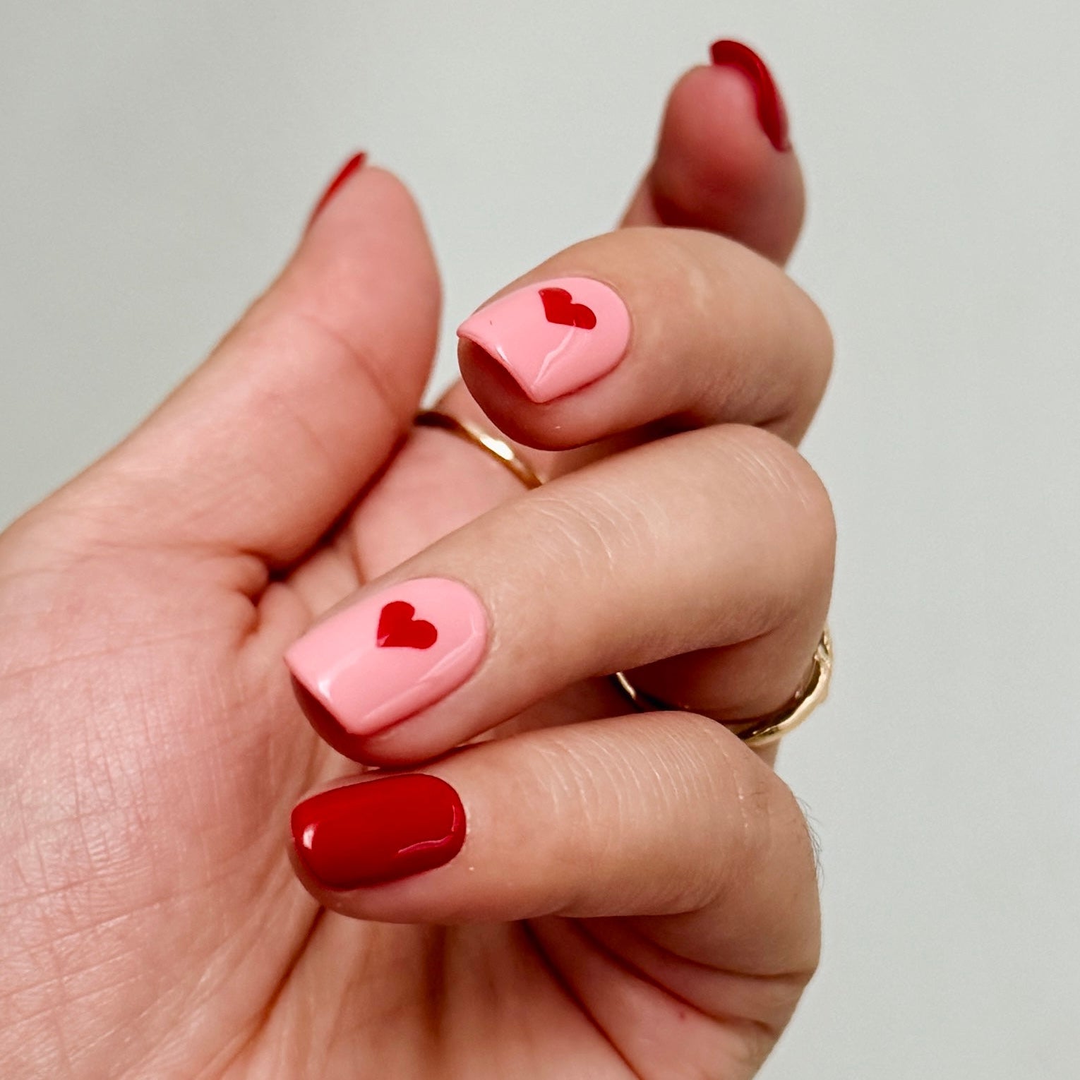 Hand with pink and red nails featuring heart designs on a neutral background