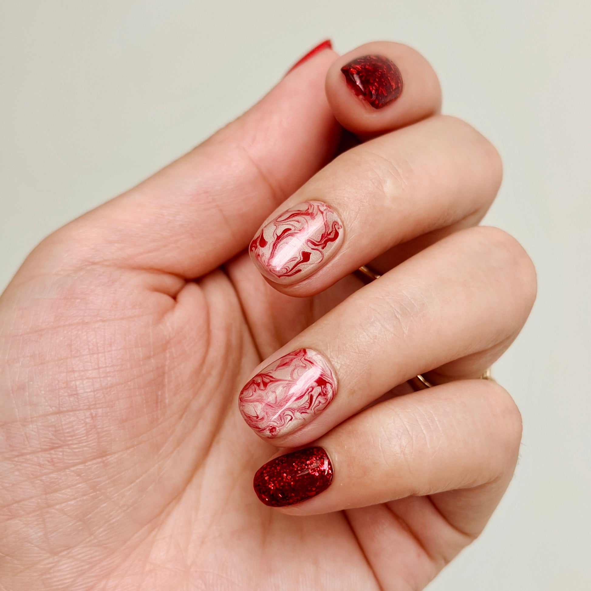 Hand with marbled red and white nail polish on a plain background