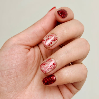 Hand with marbled red and white nail polish on a plain background
