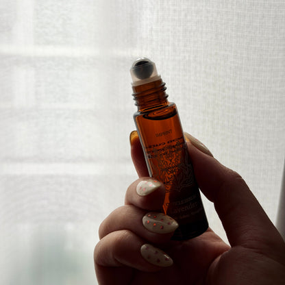 Hand holding a small brown rollerball bottle against a white background