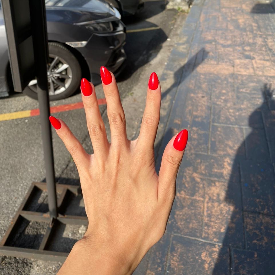 Hand with red nails in front of a street with parked cars