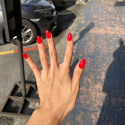 Hand with red nails in front of a street with parked cars